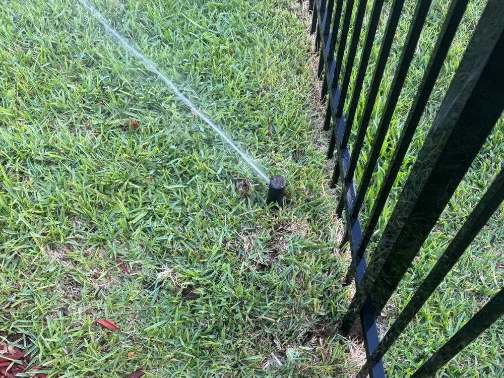 Rotor head spraying across a lawn beside a black metal fence